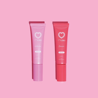 Twee tubes Muski intieme musk: Romantic (aardbei) en Seduction (witte musk) op roze achtergrond.