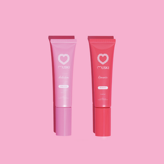 Twee tubes Muski intieme musk: Romantic (aardbei) en Seduction (witte musk) op roze achtergrond.